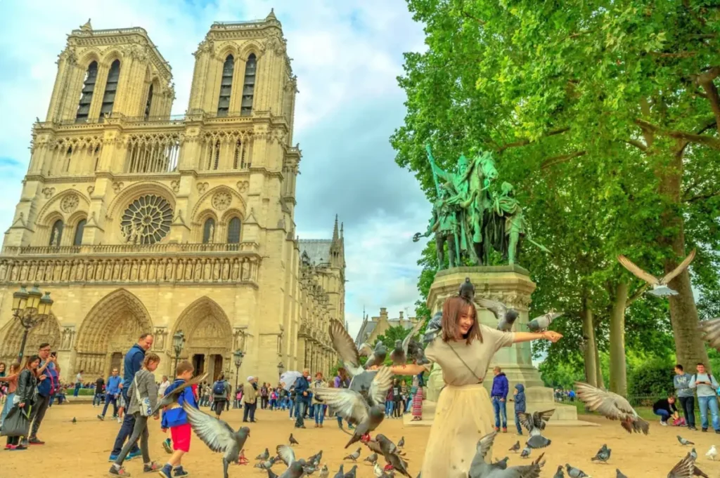 A woman joyfully playing with pigeons in the square in front of the magnificent Notre-Dame Cathedral in Paris, one of the best cities in Europe to visit.