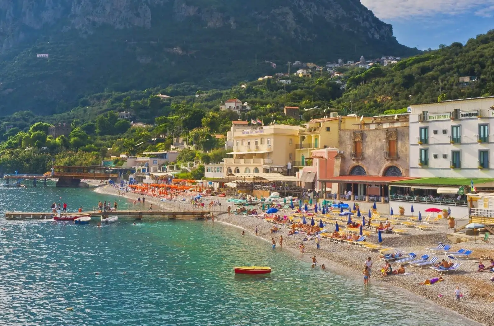A bustling beach on the Amalfi Coast, one of the best summer destinations in Europe for beach lovers, with people enjoying the sun and sea next to cliffside hotels.