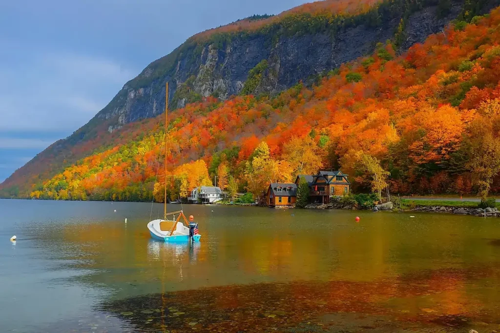 A sailboat on the calm water of Lake Willoughby in Vermont, with the steep cliffs of Mount Pisgah covered in vibrant fall foliage in the background.