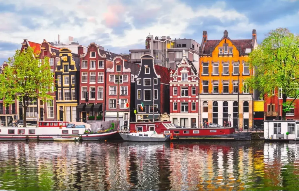 Colorful, traditional gabled houses and houseboats lining a scenic canal in Amsterdam, with their reflections in the water.