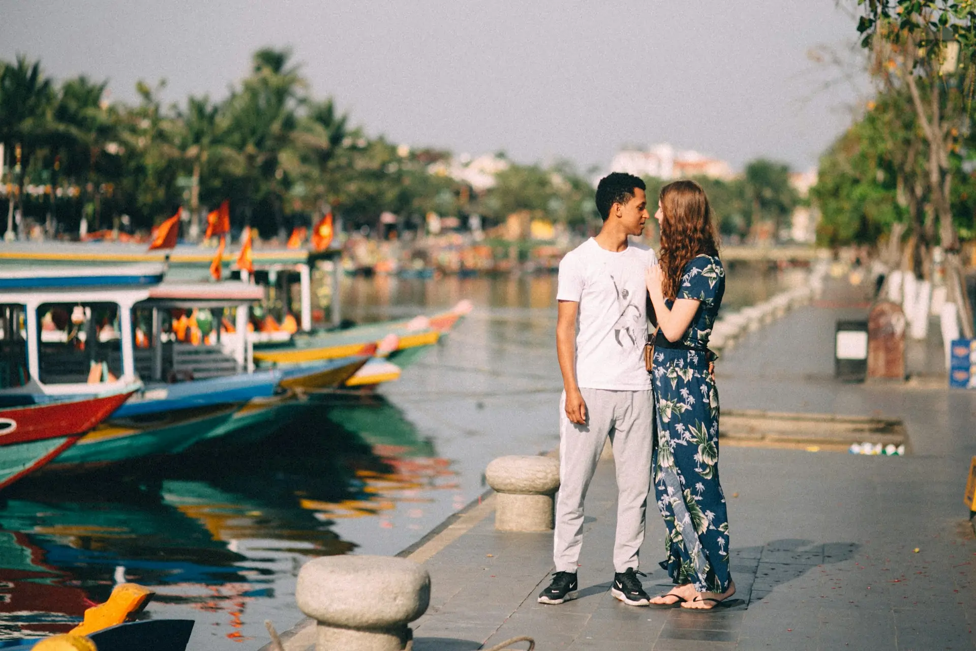 A couple on a honeymoon trip in Hoi An, one of the best cities in Asia, standing by a river with colorful boats.