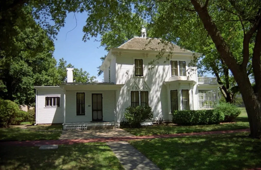 The white, two-story boyhood home of President Dwight D. Eisenhower in Abilene, Kansas, framed by green trees on a sunny day.