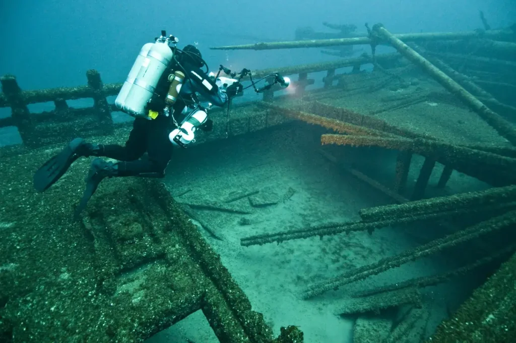A technical scuba diver with a camera exploring the coral-covered USAT Liberty shipwreck, one of the sites for the best diving in Southeast Asia.