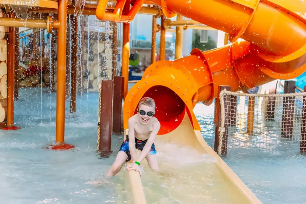 A happy young boy wearing goggles laughs as he splashes down a water slide at the Long Branch Lagoon water park, a top family-friendly attraction in Dodge City.