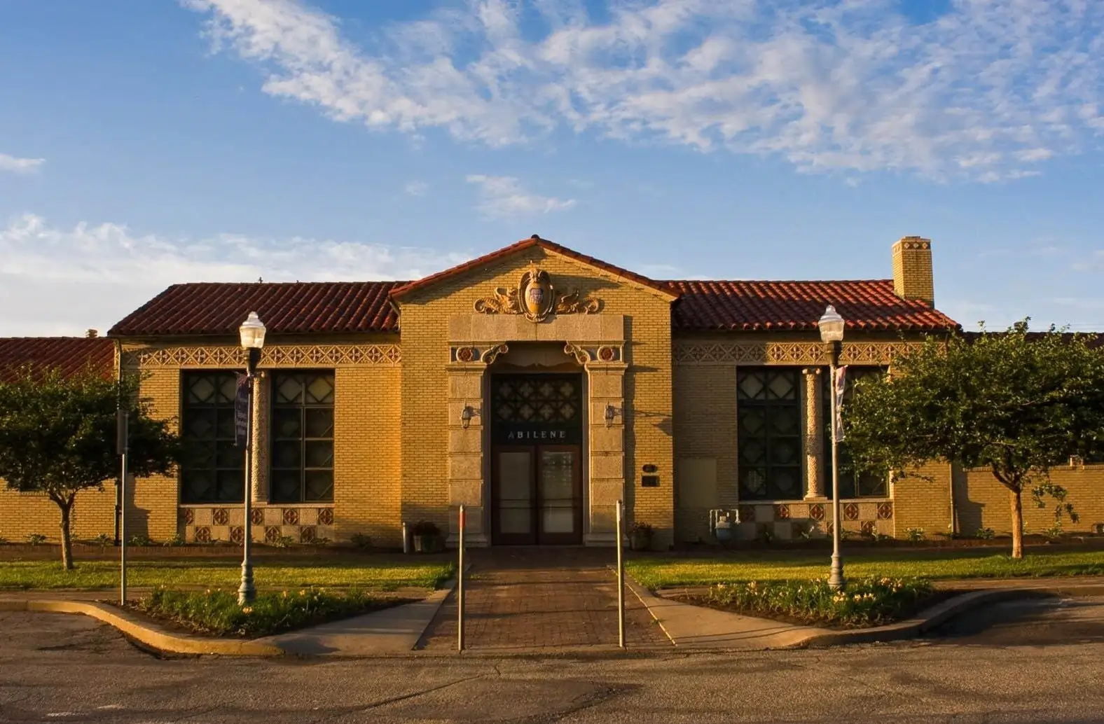 The historic Abilene Station in Kansas, a restored yellow brick Union Pacific depot now serving as the town's Civic Center, seen in the warm light of a sunny day.