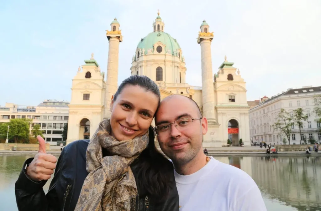 A happy couple taking a selfie in front of the magnificent Karlskirche in Vienna, Austria, one of the best honeymoon destinations in Europe for its imperial grandeur.