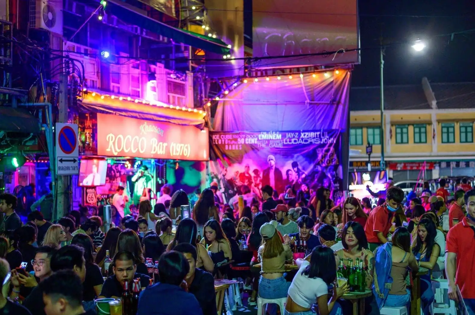 A crowded street party on Khaosan Road in Bangkok, one of the top cities in Asia for nightlife, with people at bars under neon lights.