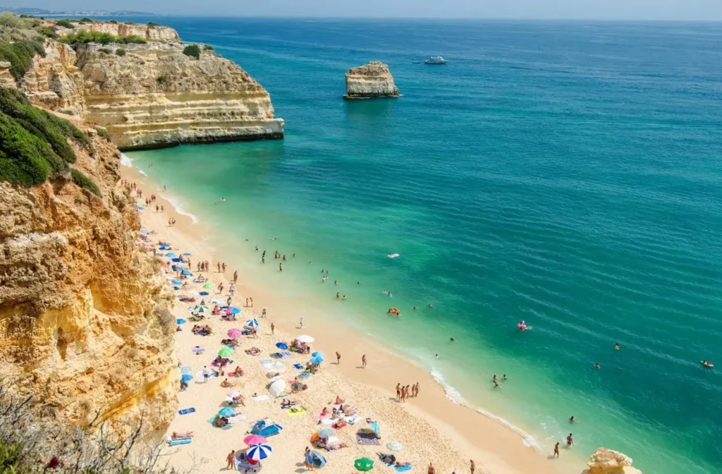 An aerial view of Praia da Marinha in the Algarve, Portugal, one of the best summer destinations in Europe, showing its golden cliffs and beach full of people.
