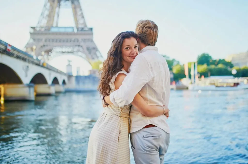 A romantic couple embracing by the Seine River in Paris, with the Eiffel Tower in the background, showcasing why it's one of the best honeymoon destinations in Europe.