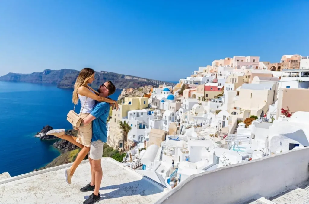 A romantic couple on a rooftop in Santorini, with the man lifting the woman, overlooking the iconic whitewashed buildings and blue Aegean Sea, a perfect example of one of the best honeymoon destinations in Europe.