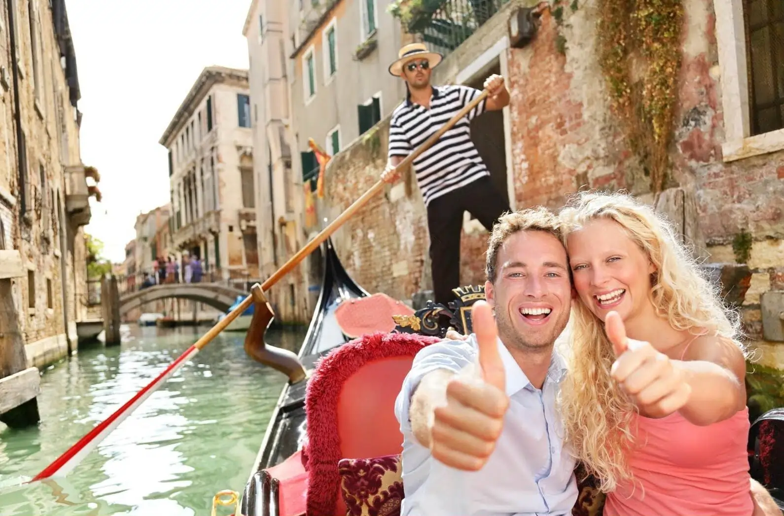 A happy couple enjoying a gondola ride in Venice, one of the best honeymoon destinations in Europe, as they smile and give a thumbs-up.