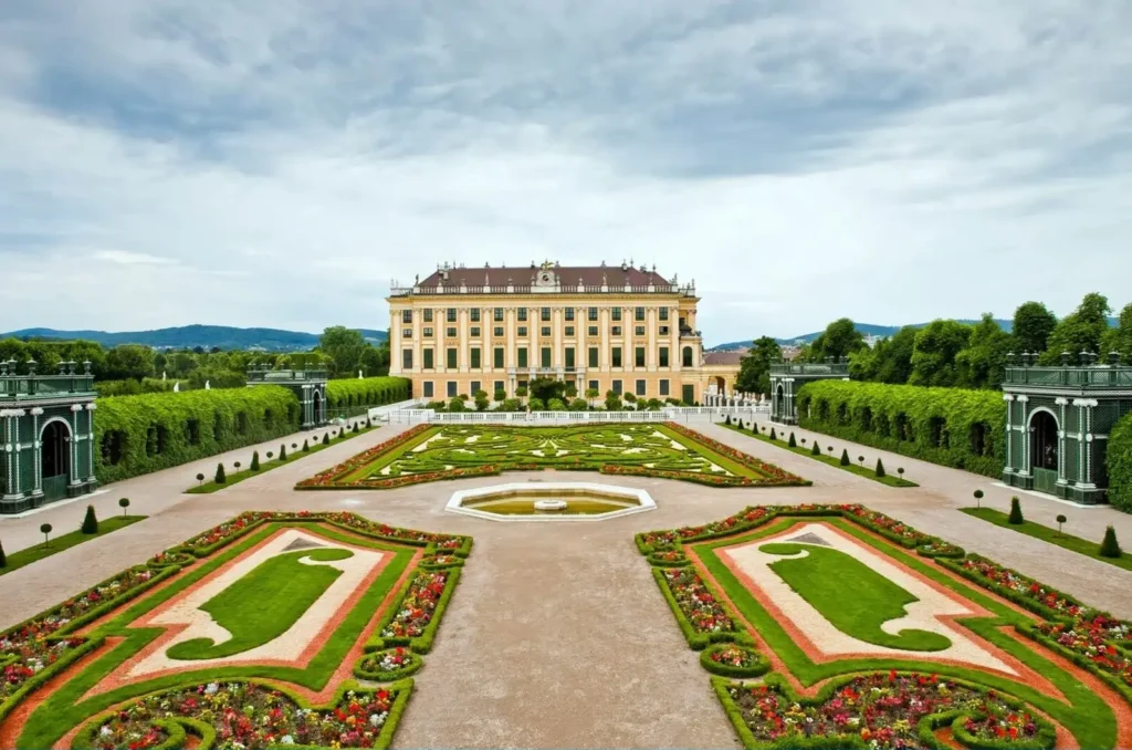 A wide view of the magnificent Schönbrunn Palace in Vienna, with its elaborate, colorful formal gardens and fountains in the foreground.