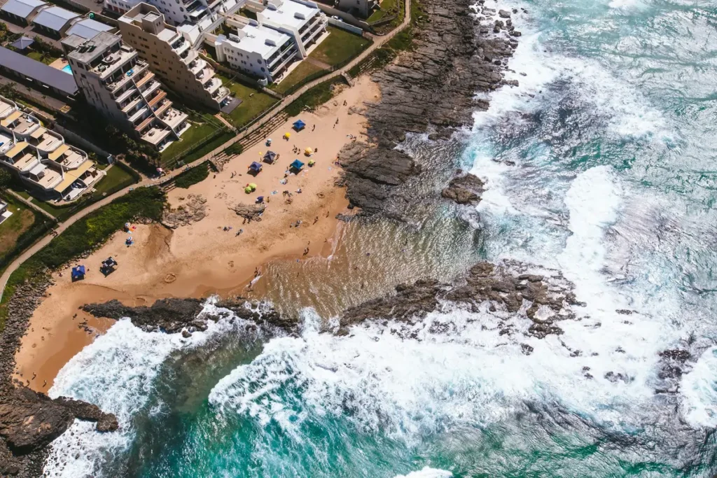 An aerial view of a beach in Durban, one of the coastal cities in South Africa, showing people on the sand next to the rocky shore and warm Indian Ocean.