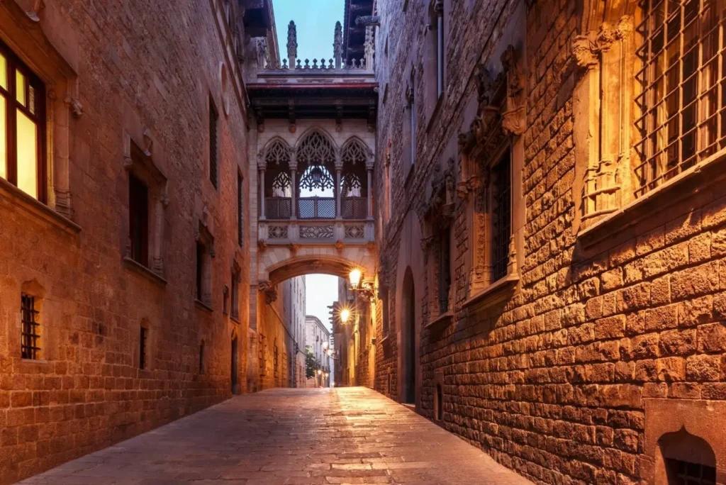 The iconic Bishop's Bridge in the Gothic Quarter, a key sight on many Barcelona tours, spanning a narrow, historic street at dusk.