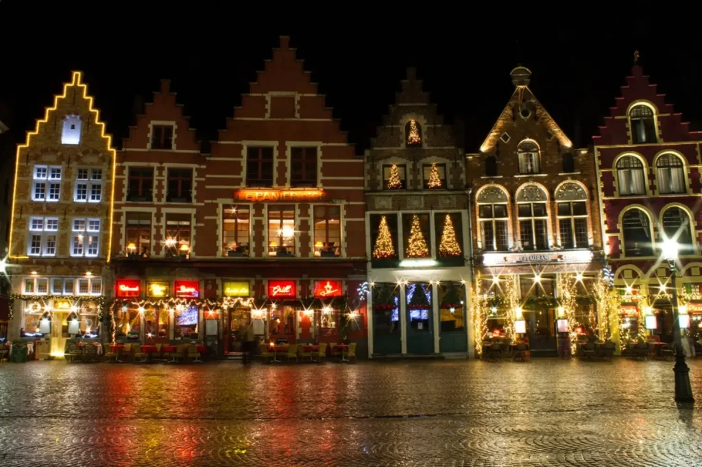 The historic gabled buildings in the main square of Bruges, Belgium, illuminated with Christmas lights at night, making it one of the best Christmas markets in Europe for romance.