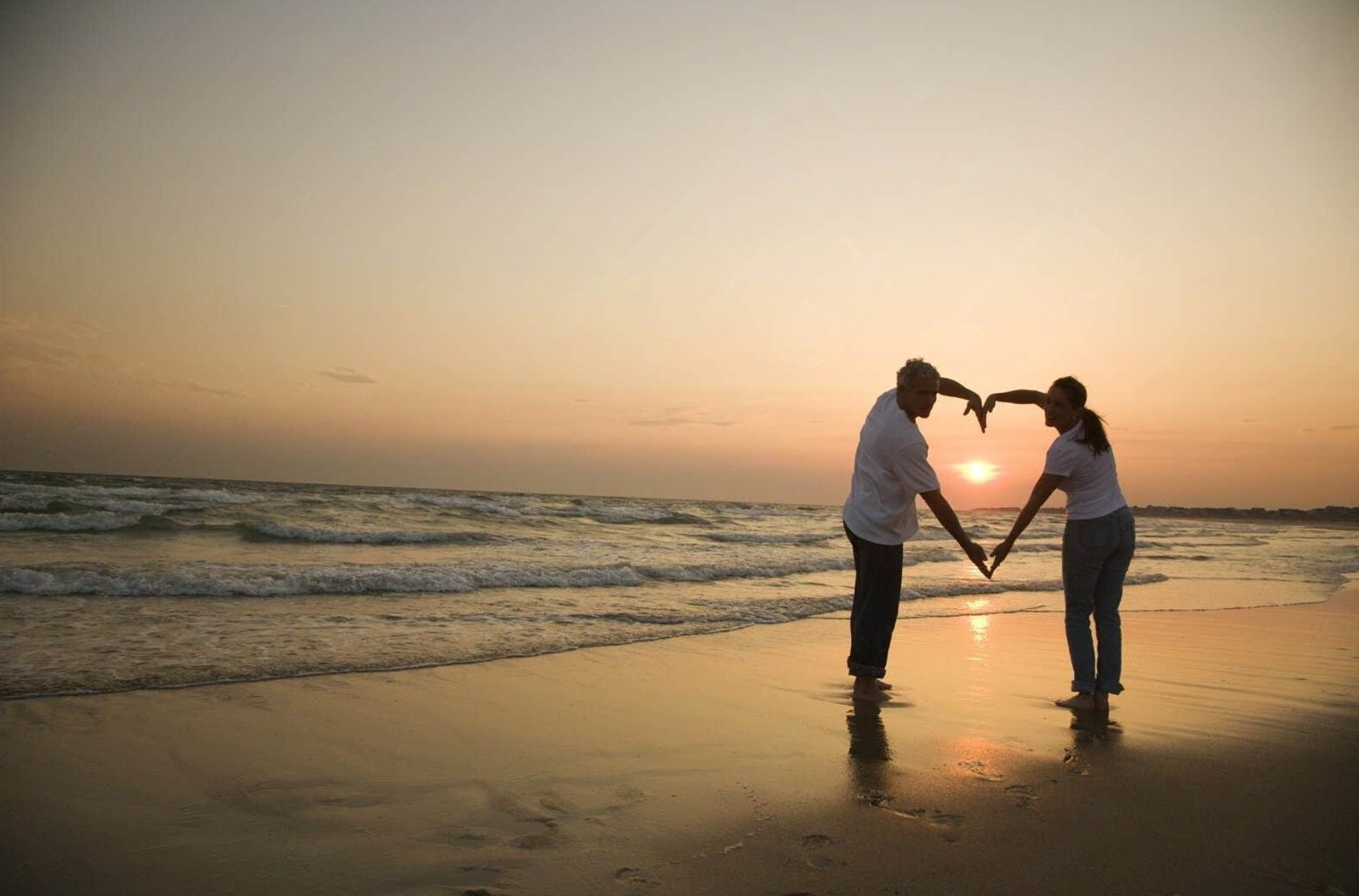 Couple walking hand-in-hand along a serene New England beach at sunset, symbolizing romance and relaxation