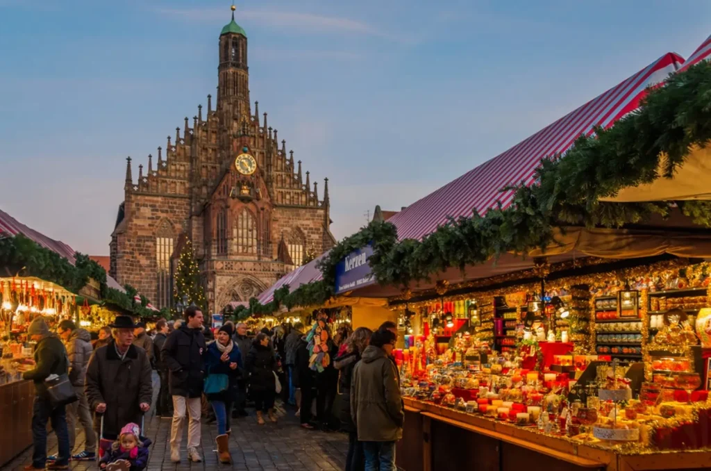 Visitors browsing stalls at the Nuremberg Christkindlesmarkt, one of the most famous and best Christmas markets in Europe, with the Church of Our Lady in the background.
